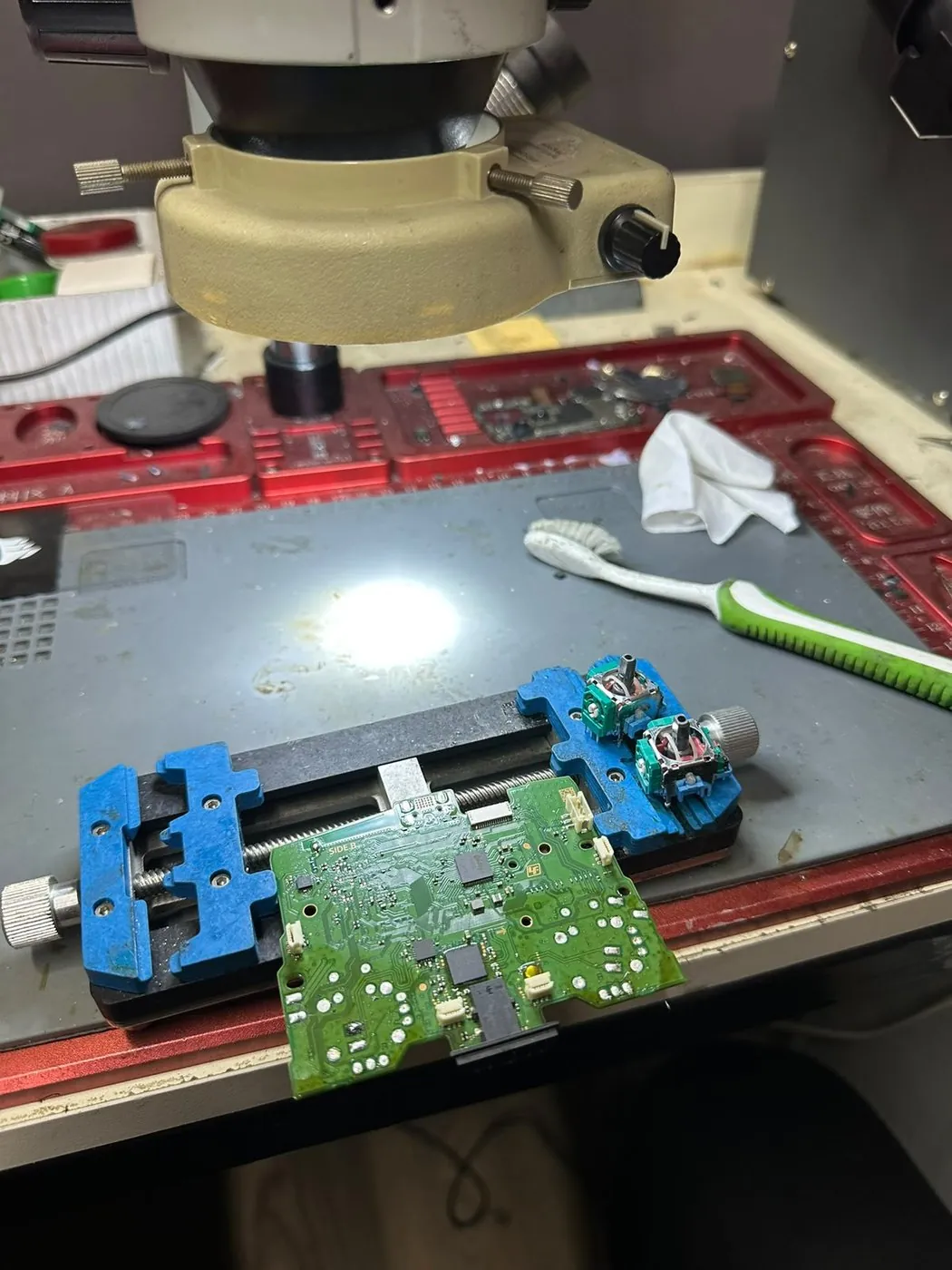 DualSense Kol Drift Onarımı — Anakart mikroskop altında, analog modüller sökülmüş